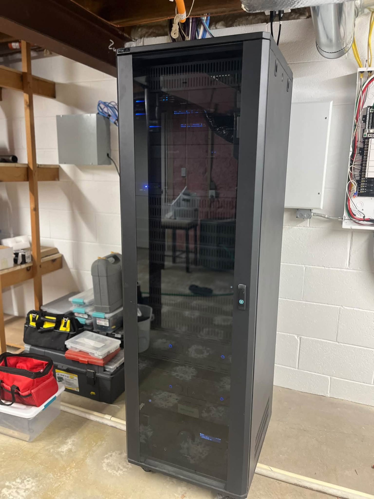 A black equipment rack cabinet standing in an unfinished basement before the surrounding wall is built.