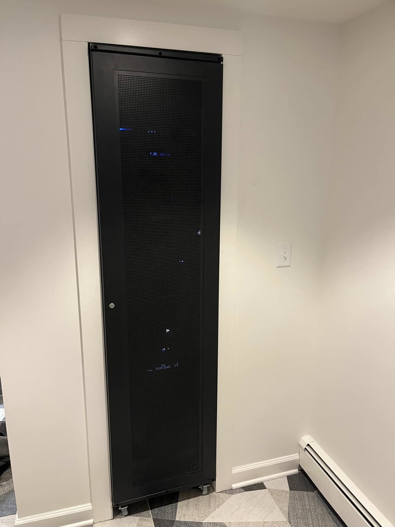 A tall equipment rack cabinet lit with blue indicator lights, standing in a closet corner.
